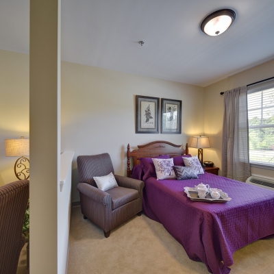 bedroom with purple comforter on bed beside a window